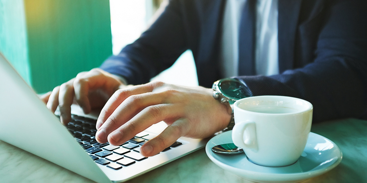 Businessman Wearing Navy Suit and Chrome Watch Using Laptop Computer Next to Empty Cup of Coffee