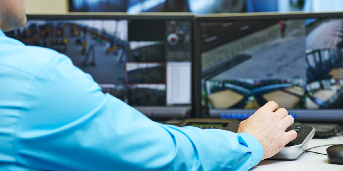 Over Shoulder View of Man in Blue Dress Shirt Viewing Security Camera Surveillance Feed on Computer Monitors