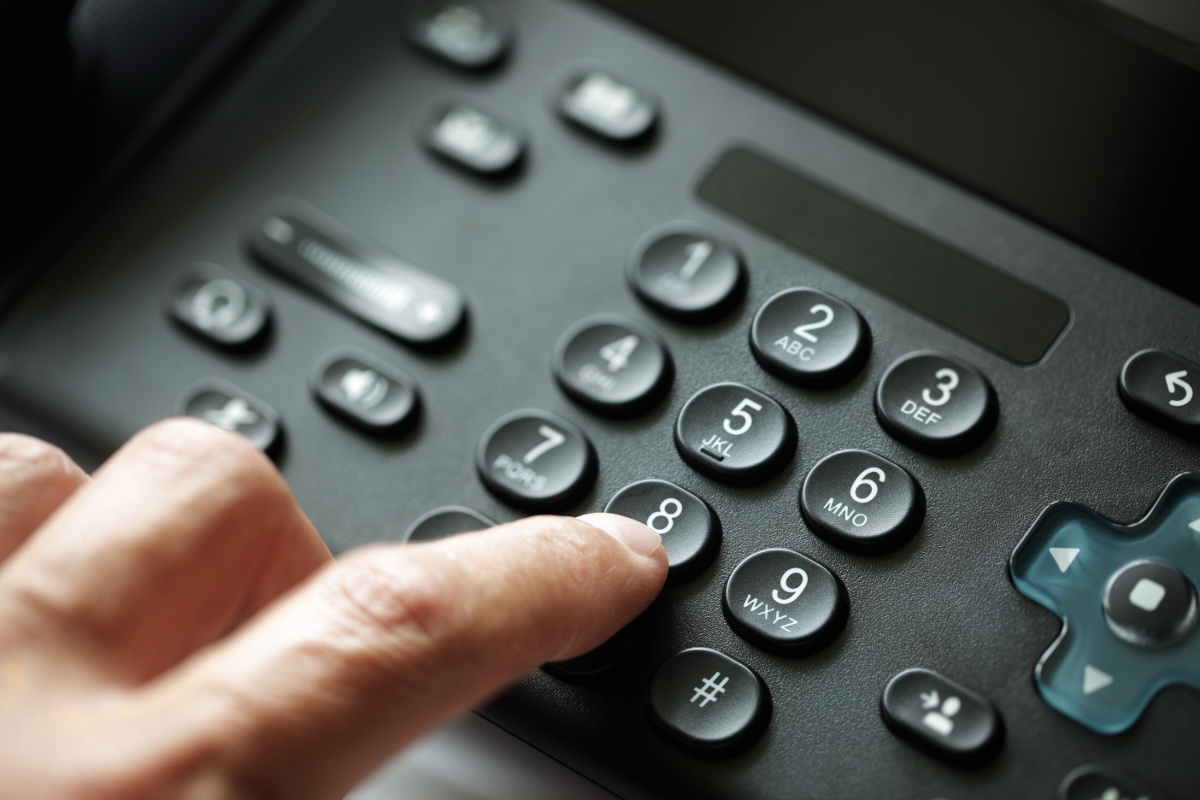 Finger pressing a key on a black business desk phone keypad